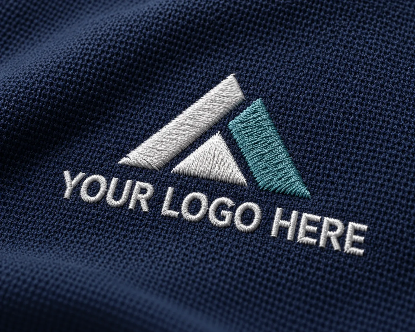 Close-up of a white and teal “YOUR LOGO HERE” design embroidered onto navy polo fabric, showing individual threads and raised stitching.